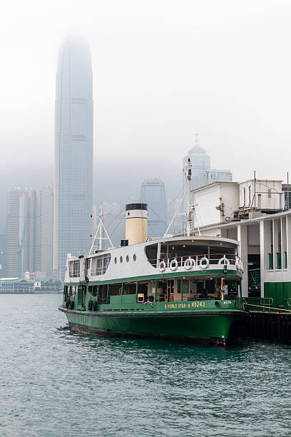 Hong Kong. China- 02.21.2025. A Star Ferry boat docked at its Tsim Sha Tsui Pier with a view of the IFC skyscraper in the background.