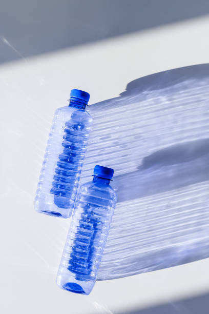 istock Transparent plastic bottles with blue caps and sun shadows on light background. Top view Water bottles at natural light. Themes of recycling, sustainability, water conservation, minimal style 2206167546