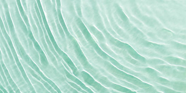 Close up view of sunlit water surface with gentle ripples with light reflections. Crystal clear water with sunlight soft wavy patterns. Abstract nature minimal background, natural textural banner