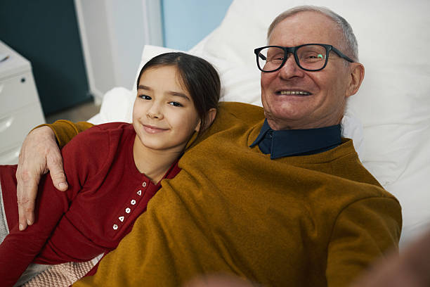 Granddad Visiting To His Granddaughter In Hospital Portrait of happy granddad smiling at camera while lying with his granddaughter on bed in the ward vietnamese old man portrait stock pictures, royalty-free photos & images