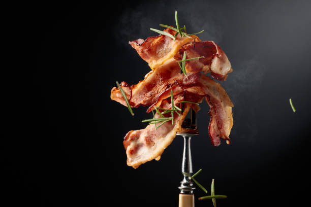 istock Fried bacon on a fork, sprinkled with rosemary, against a black background. 2206172730