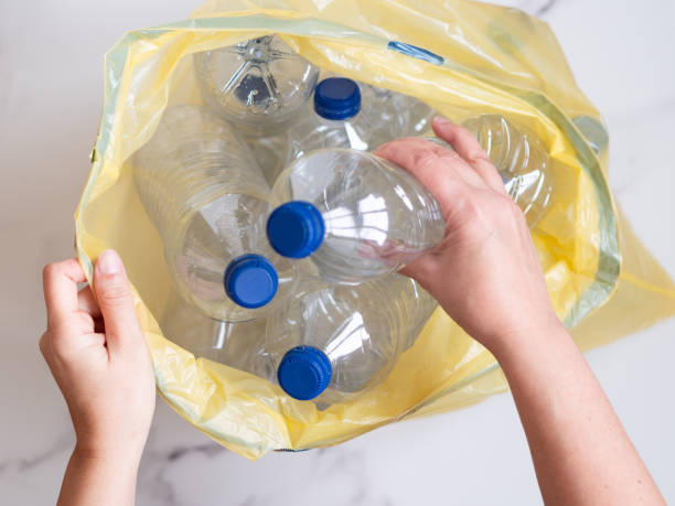istock Woman putting empty plastic bottles into yellow trash bag for recycling 2206175820