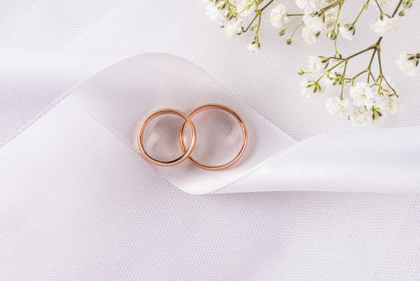 istock Two gold wedding rings lie on a chic satin white ribbon on white satin with delicate gypsophila flowers. top view. A copy space. postcard, invitation 2206180241