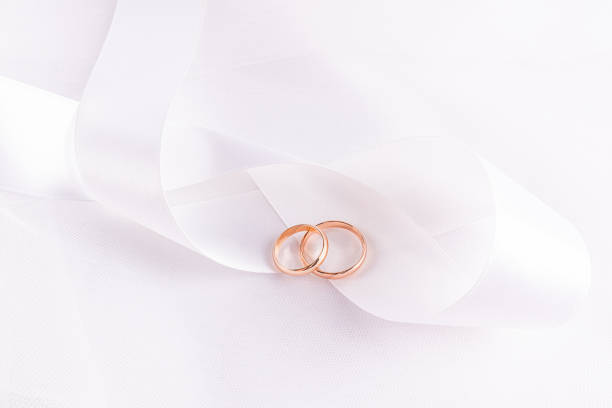 istock Chic wedding background for wallpaper design, postcard, invitation. Two elegant wedding gold rings lie on white satin wide ribbon beautifully folded. 2206180251