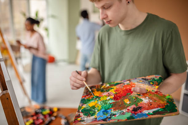 A diverse group of young artists is engaged in a vibrant art workshop. They gather to paint, express creativity, and share ideas while enjoying each other’s company in a bright, welcoming studio.