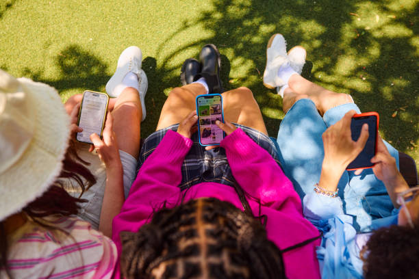 Friends using smartphones sitting on bench in park
