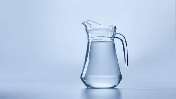 Clear glass pitcher filled with transparent water against a soft blue background. One pitcher of water. Mock up. Concept of refreshment, diet. Ample negative space for text or branding.