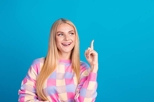 istock Smiling young woman pointing upward with a cheerful and charming expression on a bright blue background 2206185894