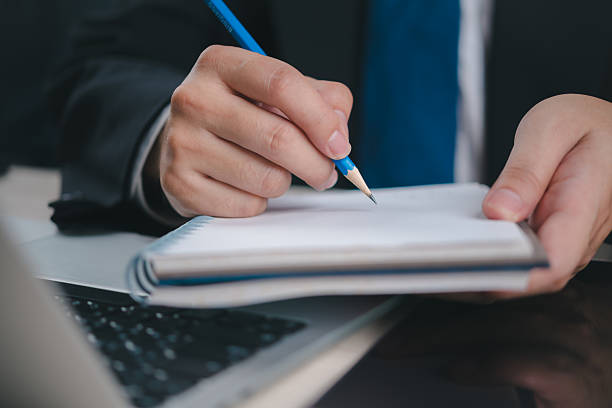istock business professional writing in a notebook with a pencil, while working on a laptop. The image symbolizes productivity and business planning in the office. 2206186997