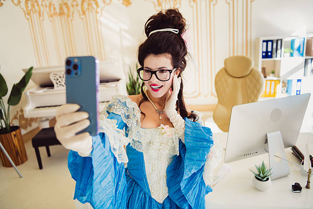 istock Young woman in historical costume taking selfie in modern office setting, blending Renaissance elegance with contemporary technology. 2206187946