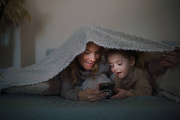 istock Mother and daughter looking at mobile phone while lying under the blanket 2206189549