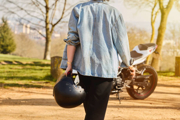 Mature woman in a leather jacket holding a helmet isolated on white background