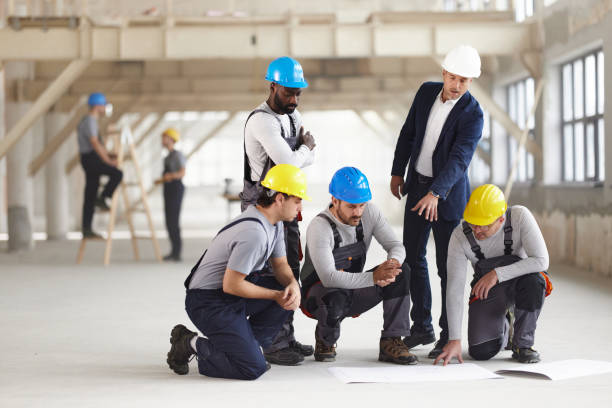 istock Male architect and his workers talking examining blueprints at construction site. 2206192482