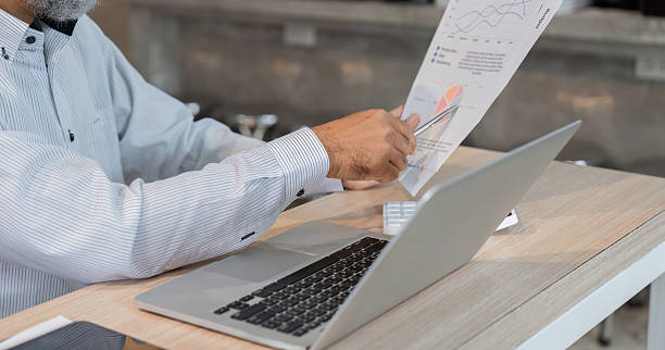 istock Business Analysis and Senior Engagement. A senior professional reviewing data reports on a laptop in a modern workspace. 2206198678