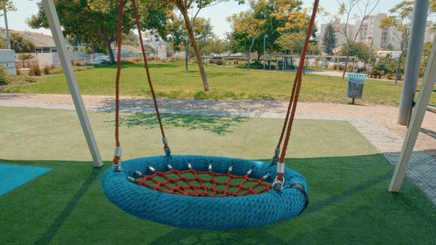 istock Empty round swing hanging in a playground surrounded by green grass and trees 2206203889