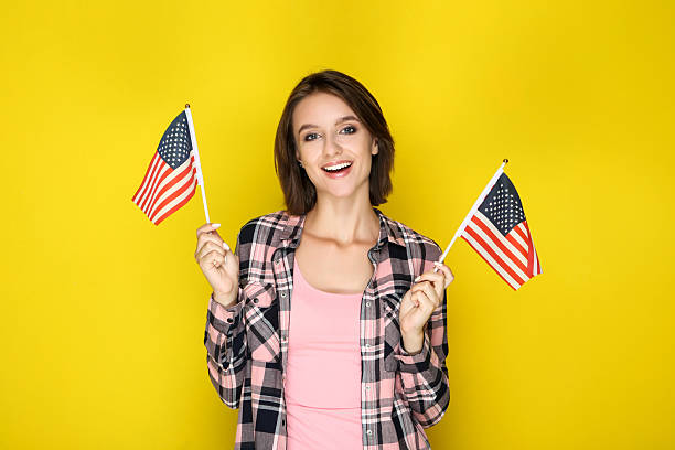 istock Young woman holding american flags on yellow background 2206205079