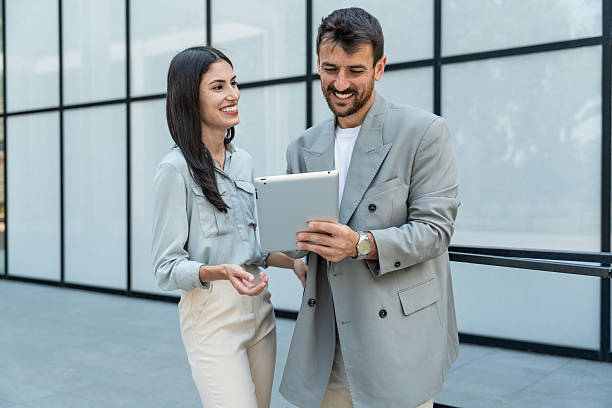 istock Two businesspeople standing outside of modern office building using digital tablet working on new project discussing and explaining business matters and smiling. Design professional occupation persons 2206205352
