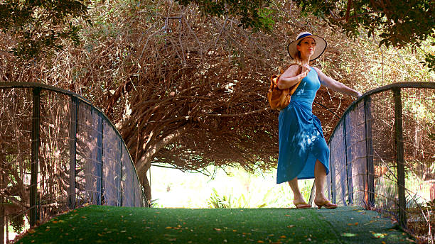 Tourist wearing blue dress and hat posing on a bridge in a botanical garden