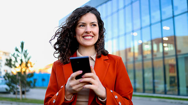 istock Smiling businesswoman using smartphone near office building 2206221771