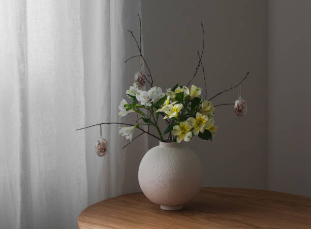istock Easter composition with fresh flowers, branches and decorative eggs in a ceramic round vase on a wooden table 2206223840