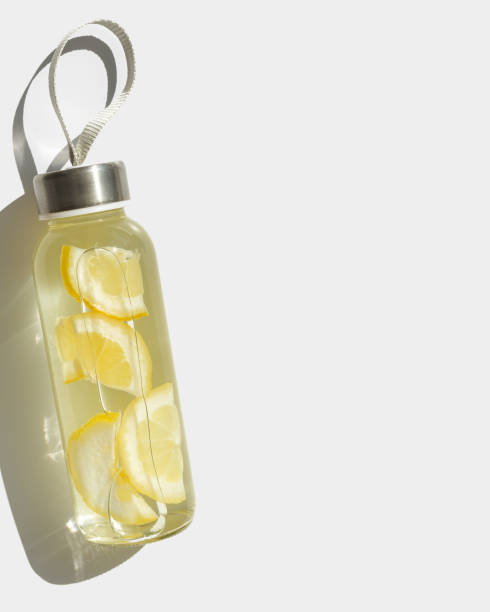 istock Cleansing and refreshing lemon water drink detox, shadow at sunlight on white with sun glare caustics. Wellness, alkaline diet, eating healthy concept. Stylish glass reusable water bottle 2206224054