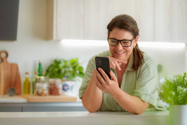 istock Relaxed woman using phone in the kitchen. Text messaging. Reading message. Sharing photos. Browsing social media 2206228468