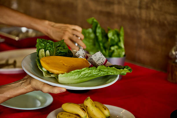 A plate of fresh fruit and vegetables, including lettuce, dragon fruit, and slices of mango, held against a table setting suggesting a healthy eating or culinary preparation theme.