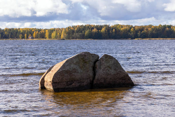 A serene natural scene of a large split rock in a tranquil lake surrounded by Autumn forest scenery