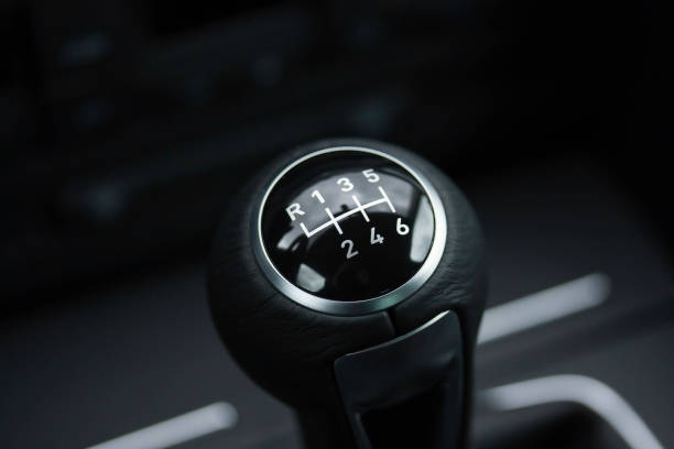 This close-up shows a manual transmission gear shift, featuring a distinctive number layout and sleek design. The sunlight reflects off the polished surface, emphasizing the craftsmanship involved in this essential component of driving dynamics.