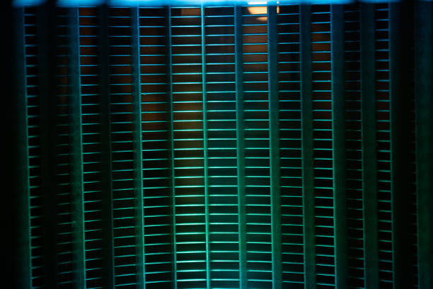 A metal grille with intricate patterns is illuminated by colorful lights in a contemporary environment. The play of colors and shadows enhances the design, creating a striking contrast against the dark background. This moment captures a blend of architecture and art.