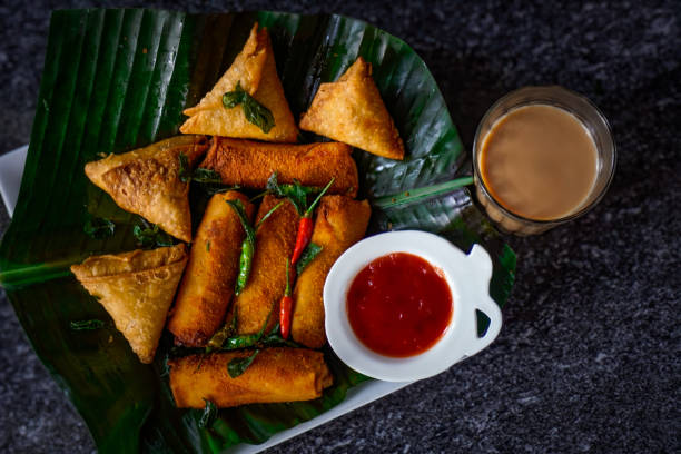 Image of top-down shot of Sri Lankan street snacks / egg rolls and samosas on banana leaf, chai tea, tangy sauces, ketchup for dipping