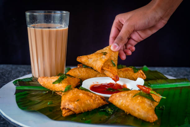 Image of Sri lankan fast food / hand dipping samosa into tomato sauce, ketchup, served with chai tea on banana leaf