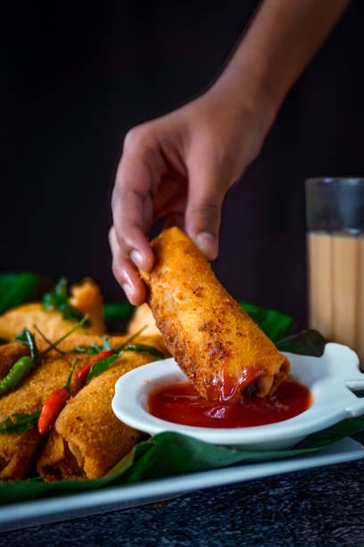 Image of close-up of sri lankan street snack / hand dipping crispy samosa and egg roll into ketchup, tomato sauce, chai tea, chilli