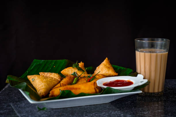 Image of Sri Lankan fast food tray / egg roll, samosa, chai tea, tomato sauce, ketchup, fresh curry leaves served on  banana leaf