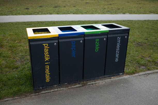 Four separate trash bins for recycling in the park, each labeled for plastic, paper, metal, and general waste. The color-coded bins support environmental efforts for waste sorting and recycling.