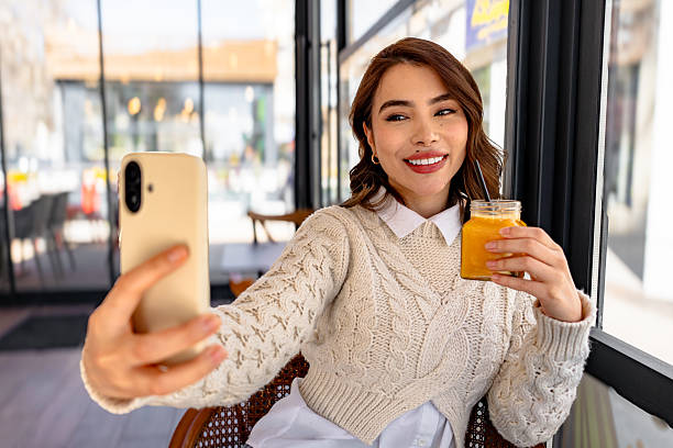 istock Young woman taking selfie while drinking orange juice in cafe 2206250977