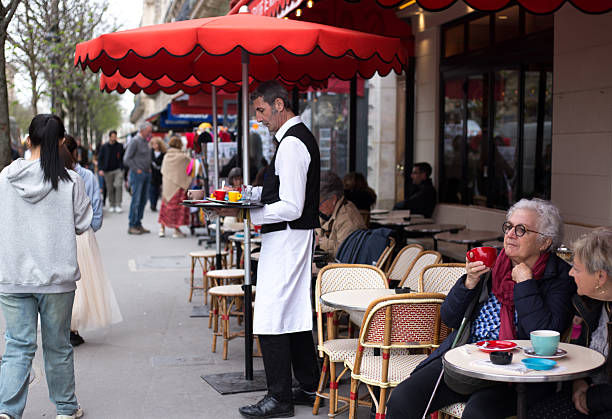 Paris, France: A waiter works at a sidewalk cafe in the 5th arrondissement as senior customers relax in the foreground.
