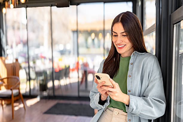 istock Smiling businesswoman using smartphone while standing at cafe entrance 2206251235