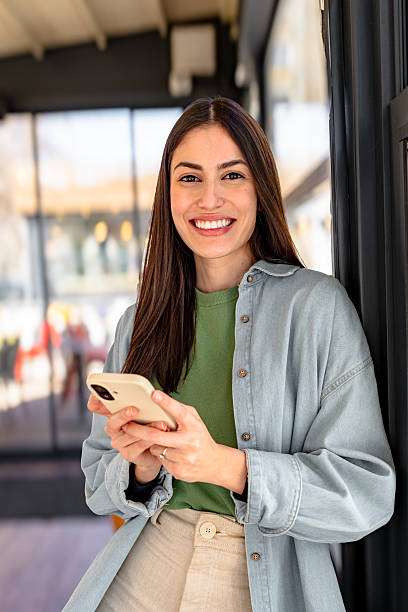 Young entrepreneur smiling and using mobile phone in front of her startup shop