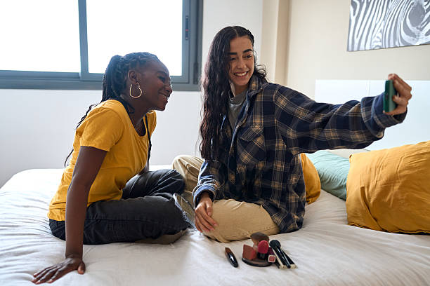 Two young women taking a selfie after applying makeup in bedroom