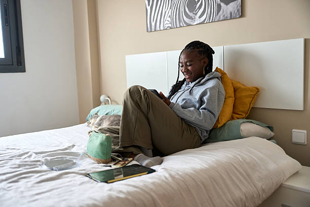 istock Young woman relaxing on bed using smartphone with cat sleeping next to her 2206255983