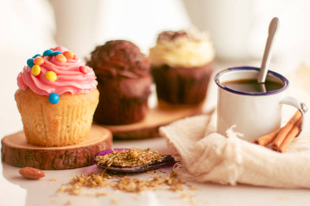 Image of afternoon coffee with milk jugs in the background and cupcakes diagonally with a cup of coffee in the image taken from the front