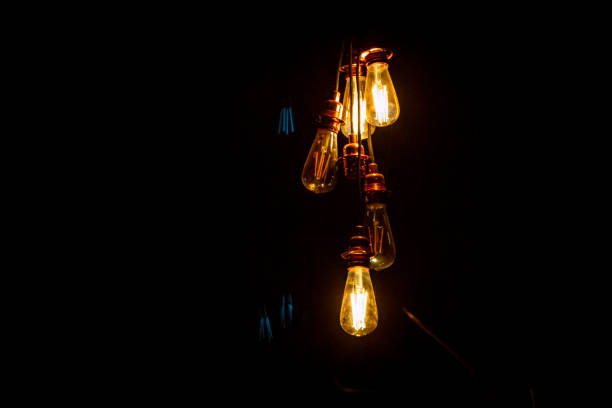 Retro style light bulbs hanging from the ceiling, shining in the dark with black background