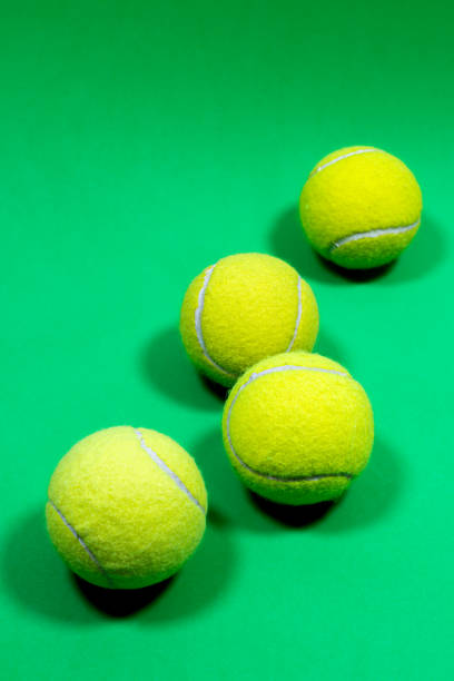 Four yellow tennis balls, in a row on a green ground.