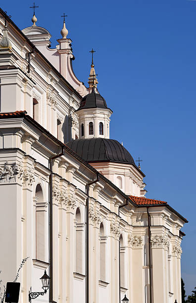 The image captures a powerful perspective of a grand white church or cathedral, viewed from behind. The massive structure ascends diagonally on the left side, emphasizing its monumental presence. On the right, the clear blue sky enhances the sense of divine grandeur, making the architecture feel even more imposing and awe-inspiring.