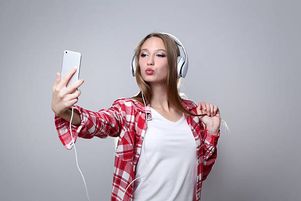 Young woman with headphones making selfie on grey background
