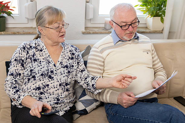 Senior couple Reviewing Important Documents at Home, Showing Concern and Togetherness While Sitting on Sofa, Engaged in Deep Discussion About Financial Matters. High quality photo