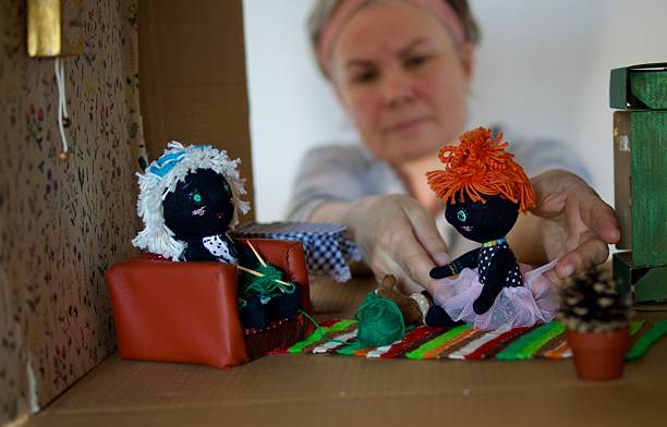 A woman arranges dolls in a doll's house made from a cardboard box