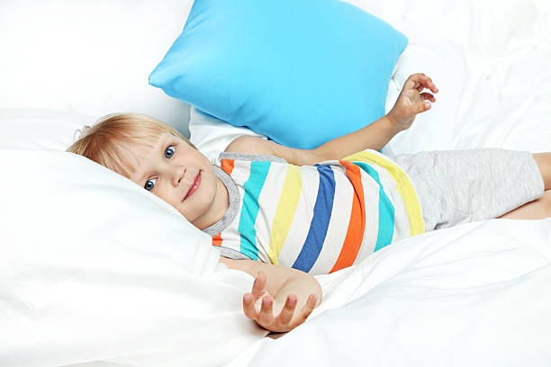 Little boy lying in white bed with blue pillow