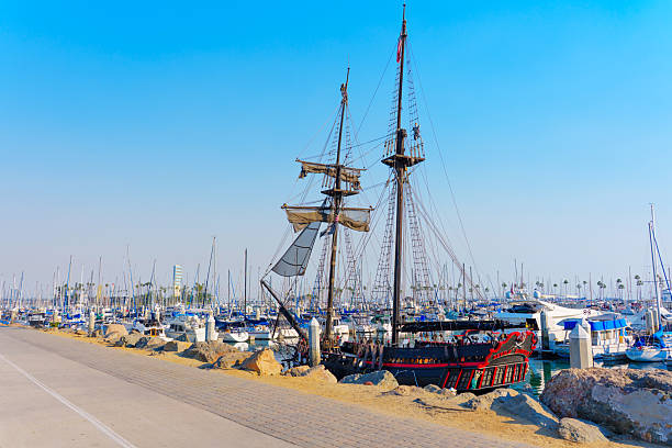 Long Beach, California - January 11, 2025: Detailed view of the Devil’s Gauntlet pirate ship docked in Shoreline Village, Long Beach, surrounded by numerous yachts under a clear blue sky during the daytime.